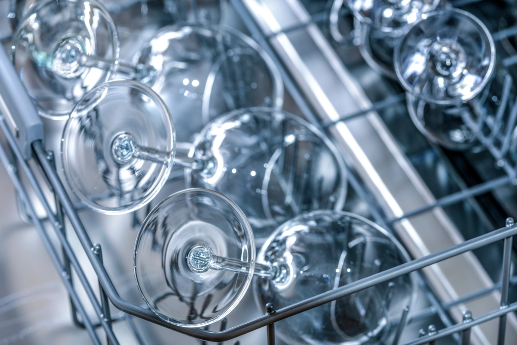 Stemmed wine glasses lying tipped over on their bowls across a dishwasher rack