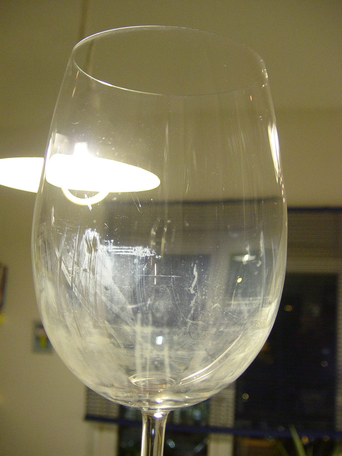 A stemmed wine glass held up in front of a lamp, the bowl covered in a dull streaky film