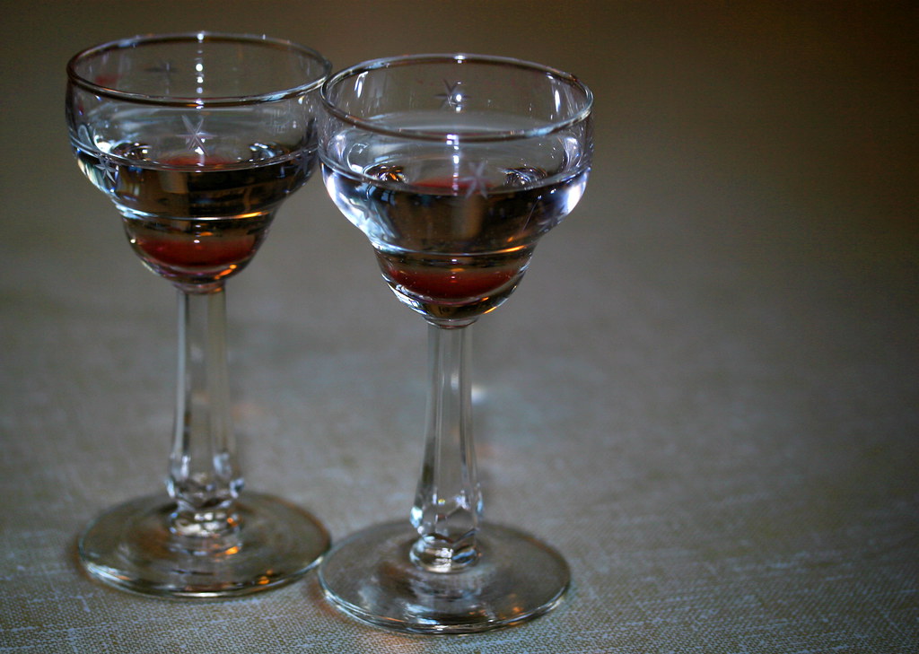 Two small stemmed glasses standing side by side on a pale cloth, each about a third full