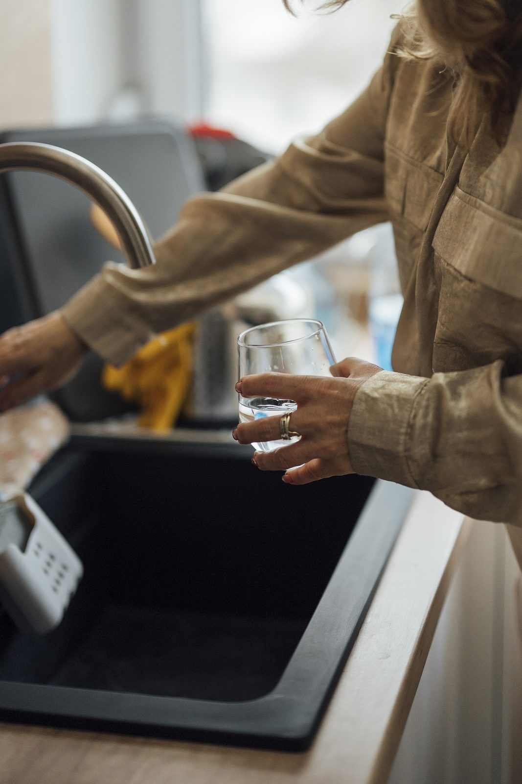 A woman at a kitchen sink washing a clear drinking glass, holding it in one hand