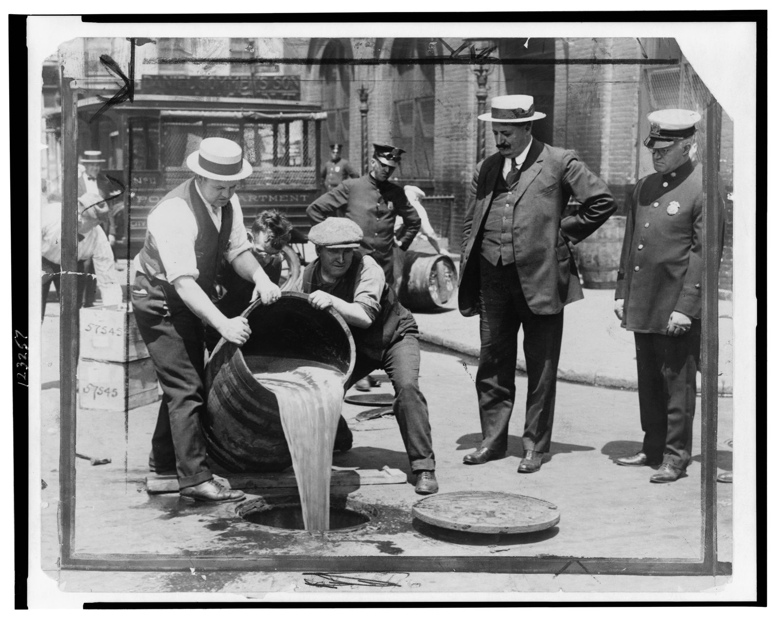 Prohibition agents pouring confiscated liquor into a New York City sewer after a raid, the Deputy Police Commissioner watching